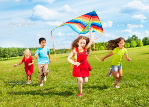 Group of four kids running in the park with kite happy and smiling on summer sunny day